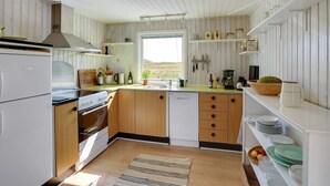 Een keuken met houten kastjes, een fornuis, een spoelbak en een raam met uitzicht op een landschap.