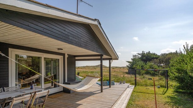 Een modern huis met een houten terras, een hangmat en een tuin.