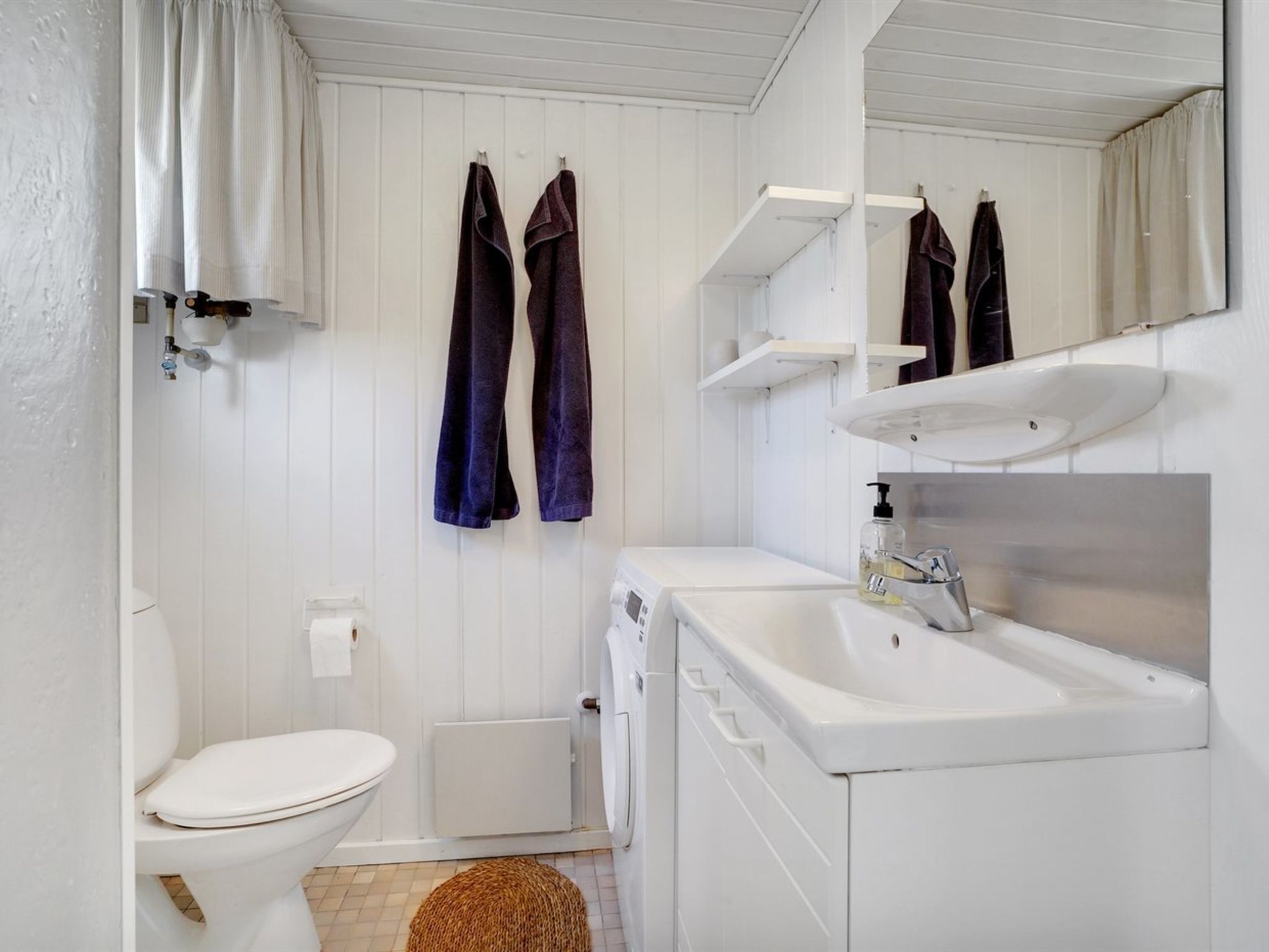 Ein kleines, weißes Badezimmer mit Toilette, Waschbecken und Spiegel. Zwei Handtücher hängen an Haken.