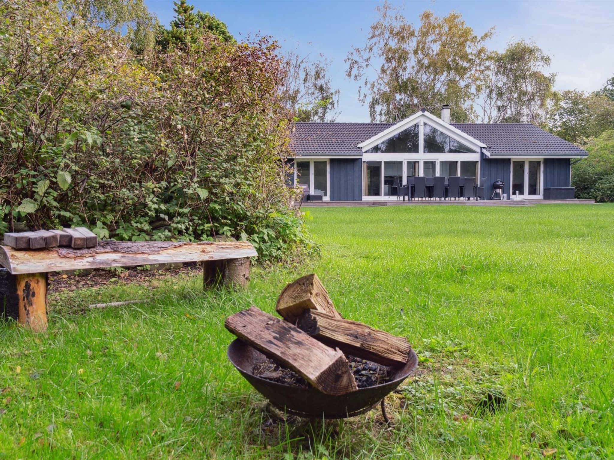 A modern house with a large lawn, a fire pit, and a bench.