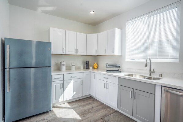 Una cocina moderna con armarios blancos, un refrigerador azul y una ventana con persianas.