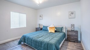 Un dormitorio con cama, dos mesitas de noche, ventilador de techo y una ventana con persianas.