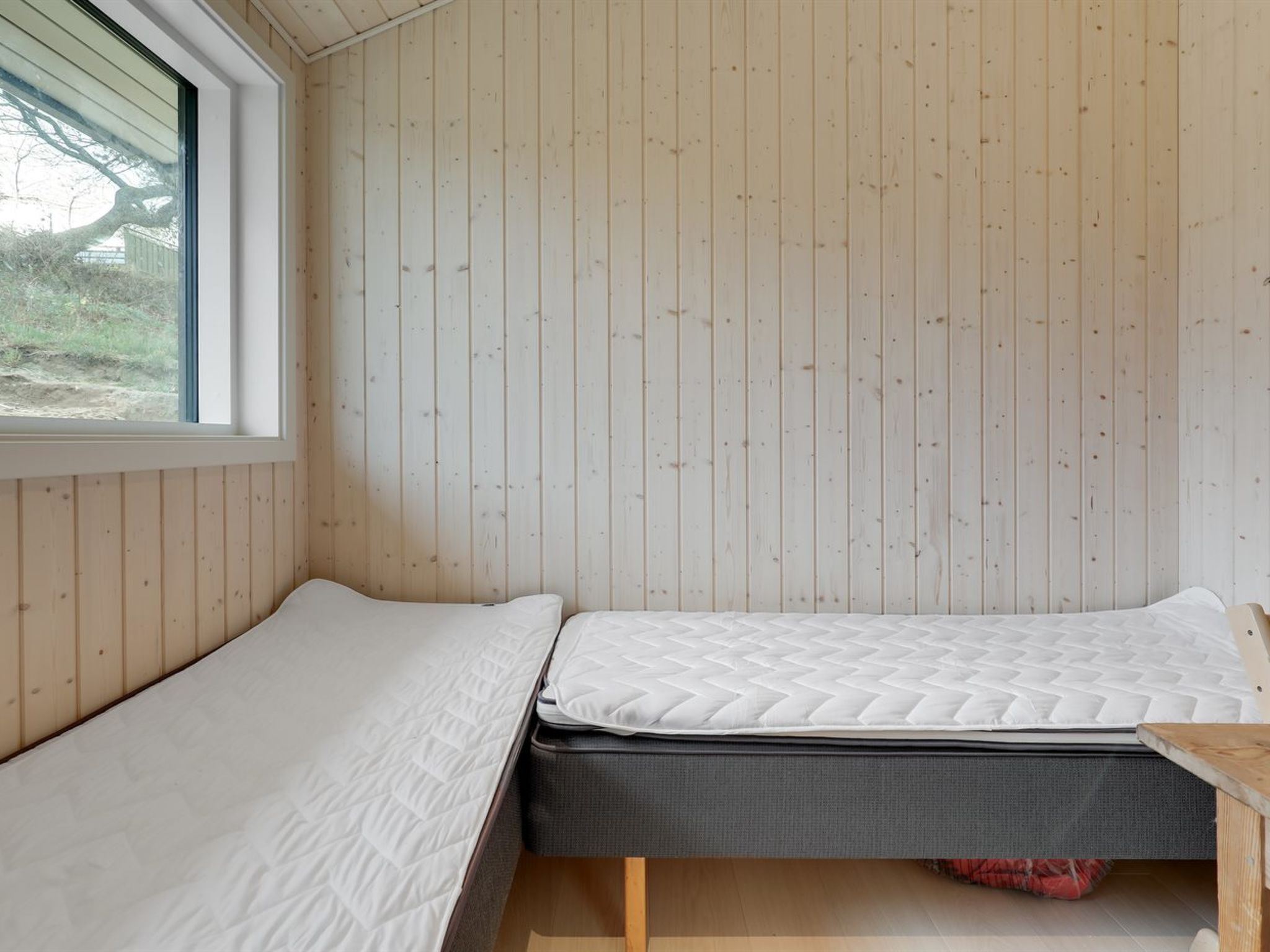 A small, single-bed room with a wooden slatted ceiling and a window.