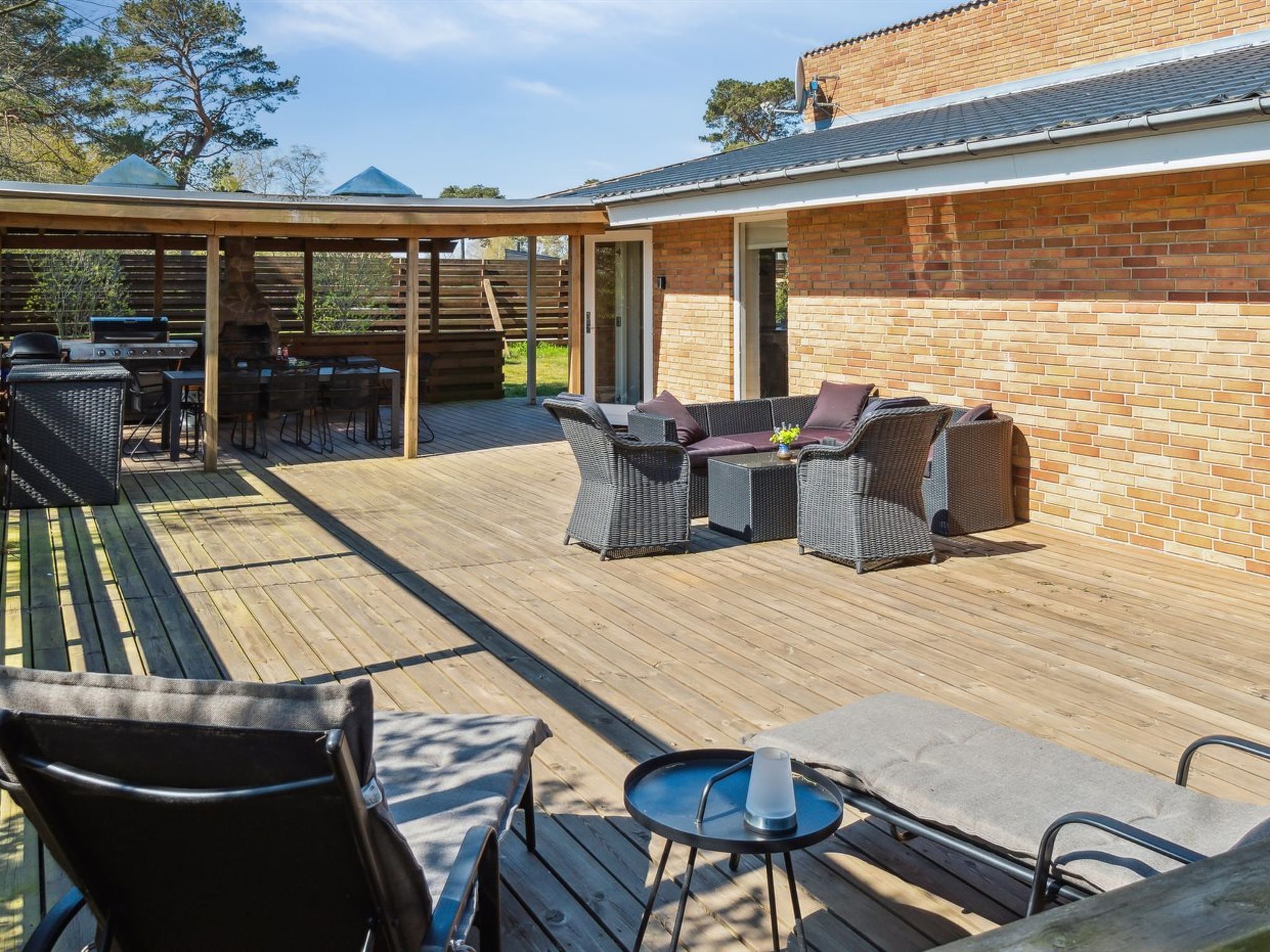 An outdoor patio with a wooden deck, wicker furniture, and a barbecue area.