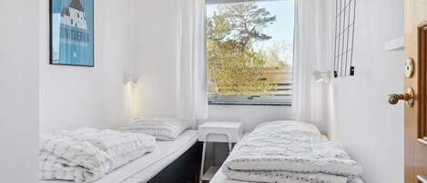 A small, clean room with two beds, a window with a view of trees, a small table, and a door.