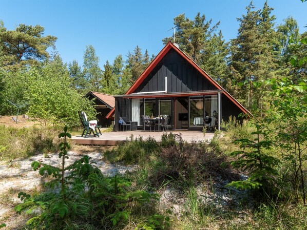 Una cabaña moderna con techo rojo y ventanas amplias, rodeada de un bosque denso.