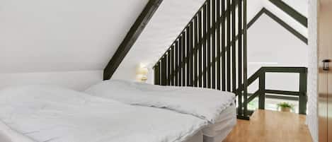 A bedroom with a sloped ceiling, a bed, a nightstand, and a window with a view.