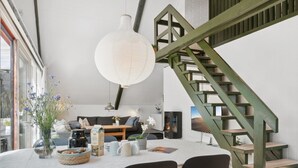 Moderni sisustus, jossa on ruokailutila pyöreän pöydän, mustien tuolien ja riippuvalaisimen kanssa. Taustalla näkyy puinen kaide, joka kuuluu portaisiin.