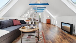 Un loft spacieux avec un plafond haut, des poutres apparentes, une grande fenêtre, un canapé, une table basse et un téléviseur à écran plat.