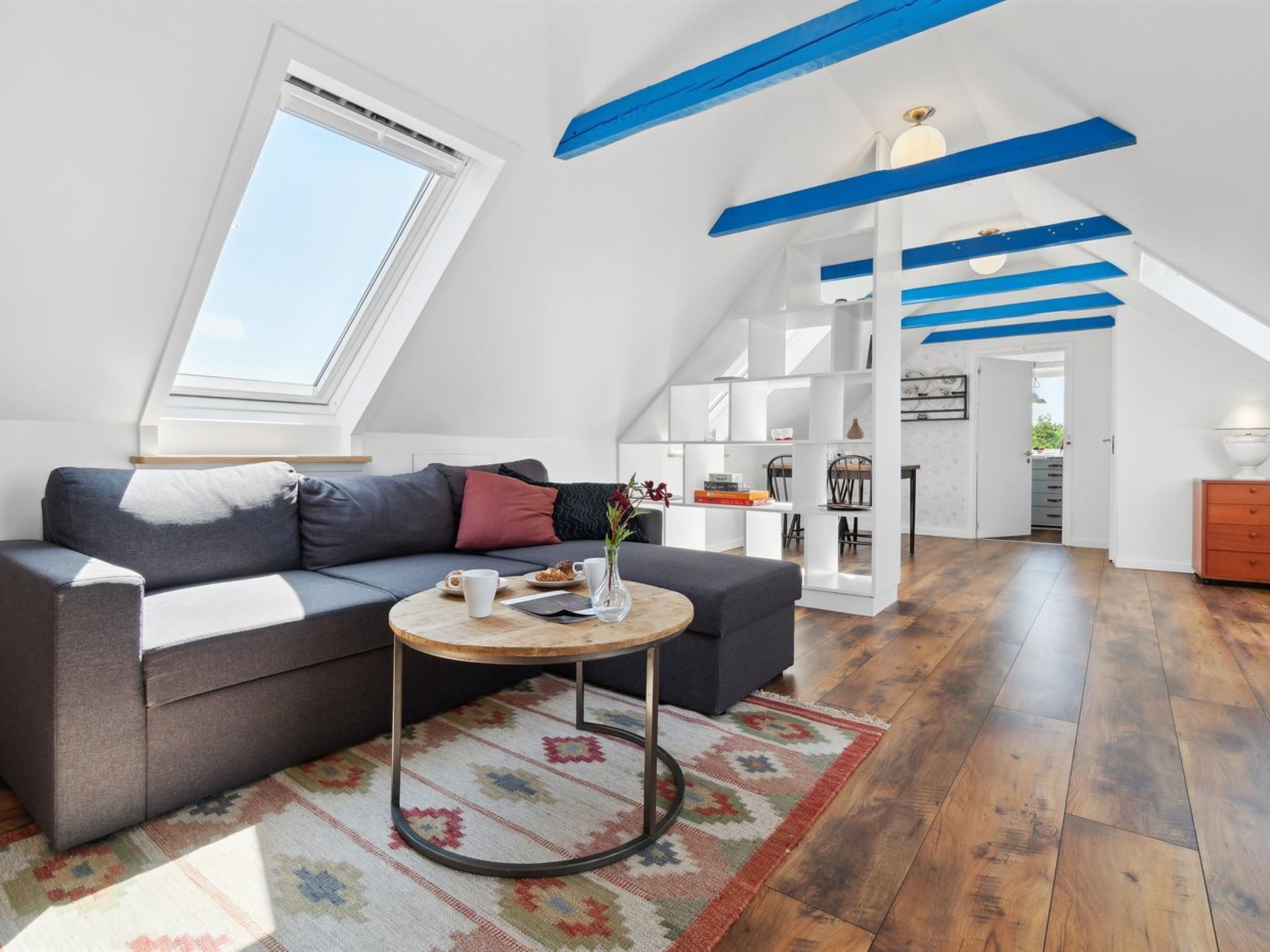 Ein modernes Loft-Apartment mit schrägverdachter Decke, einer eingebauten Bücherwand, einem runden Couchtisch und einem großen Fenster für natürliches Licht.