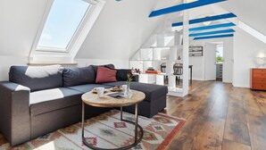Un appartement moderne de style  « loft », doté d’un plafond en pente, d’une bibliothèque intégrée, d’une table basse ronde et d’une grande fenêtre laissant entrer la lumière naturelle.