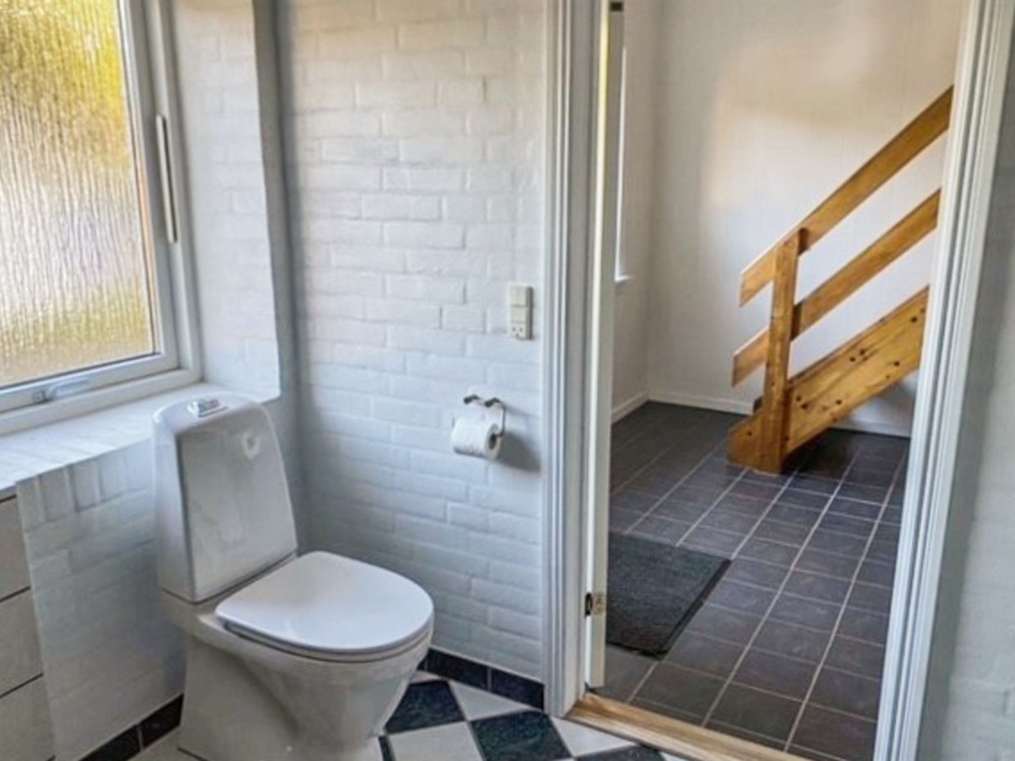 A small bathroom with a toilet, a window, and a wooden staircase leading to another room.