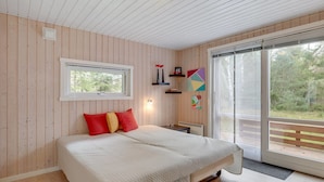 Een slaapkamer met een bed, een raam, een wandplank met decoratieve objecten en uitzicht door een schuifdeur.