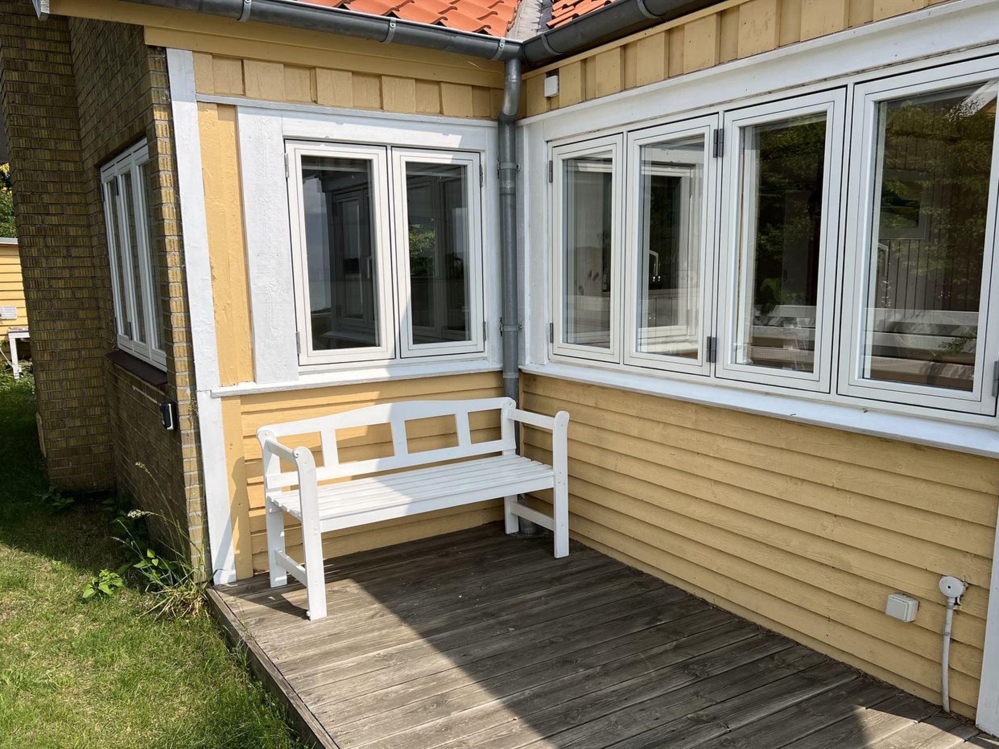 A corner of a building with a white bench, a window, and a door.