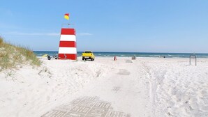 Une plage avec un phare aux rayures rouges et blanches, un véhicule jaune et des empreintes de pas qui mènent à l’eau.