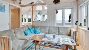 Un salon chaleureux avec un grand canapé d’angle, une table basse en bois et une vue sur la mer grâce à de grandes fenêtres.