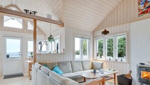 L’intérieur d’un chalet accueillant, avec un plafond en bois, de grandes fenêtres, un canapé, une table et une cheminée.