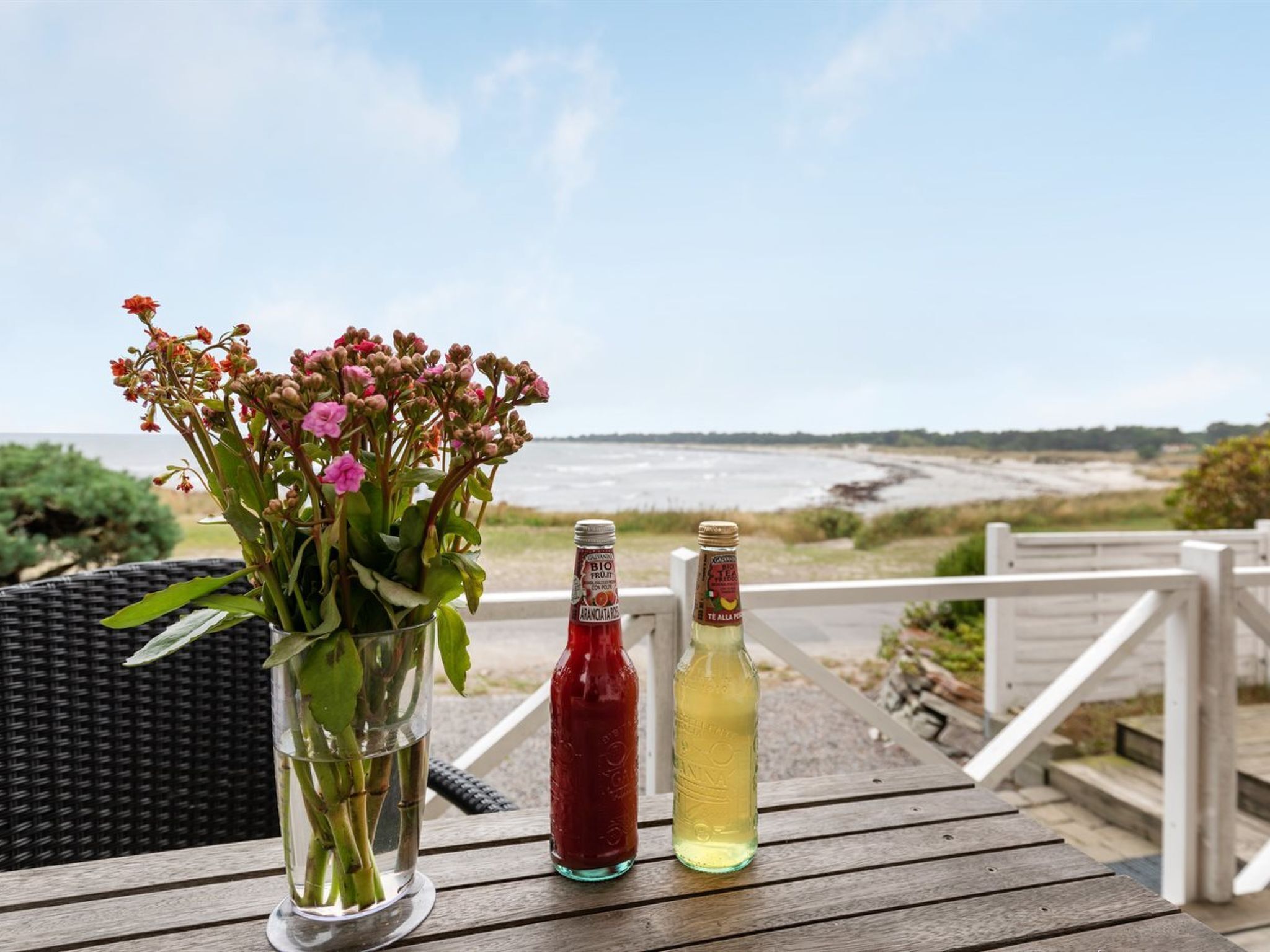 Ett bord med en vas med blommor, två flaskor med dryck och utsikt över stranden.
