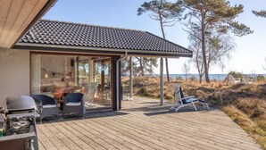 Ett trädäck med utemöbler, en grill och en glasdörr som leder till en täckt uteplats.