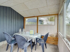 Un patio techado con una mesa, sillas, un ventanal y vistas al exterior.