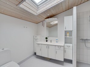 Un baño moderno con tragaluz, muebles blancos y zona de ducha.