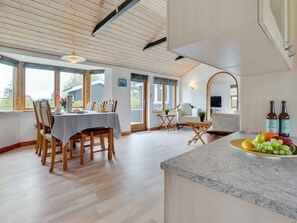 Una cocina amplia con suelo de madera, un comedor con mesa y sillas, y un frutero sobre la encimera.