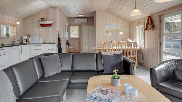 A modern cabin interior with a wooden ceiling, a dining area with a wooden table and chairs, a black leather sofa, and a kitchen with white cabinets. - "Aneline" - 700m from the sea by Interhome (Saltum)