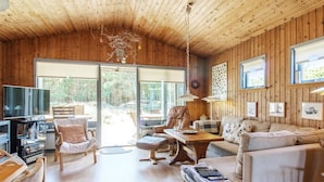L’intérieur chaleureux d’un chalet avec des murs en bois, une grande télévision et un coin salon confortable comprenant un canapé et des fauteuils.