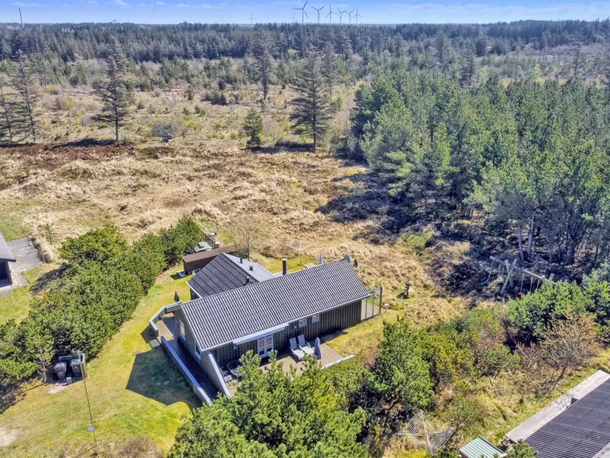 A modern house with a flat roof, surrounded by a forest and a grassy field.