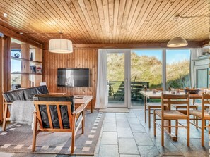 Interior em madeira com sofá, televisão, mesa de jantar e cadeiras.