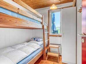 A bunk bed room with a wooden ladder, a small wooden stool, and a window with a view.
