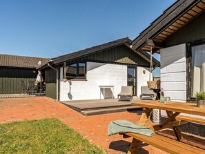 Un espace patio avec une table et des chaises en bois, une jardinière suspendue et un petit coin salon extérieur.