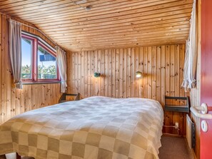 Une pièce aux murs lambrissés, avec un lit, une fenêtre et une lampe fixée au mur.