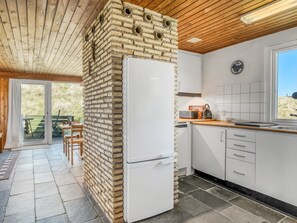 Une cuisine moderne avec un réfrigérateur blanc, un plafond en bois et une vue sur l’extérieur.