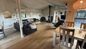 Un vaste espace de vie comprenant un canapé en cuir noir, une table à manger en bois avec des chaises, et une grande fenêtre offrant une vue sur l’extérieur.