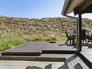 Une terrasse en bois avec une table et des chaises, donnant sur une colline verdoyante.