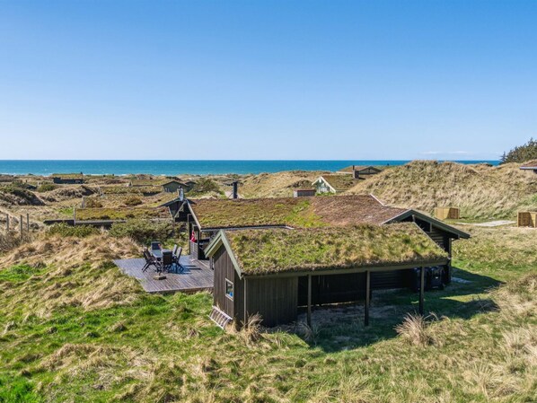 Une zone côtière avec des constructions recouvertes d’herbe, une terrasse en bois avec des sièges et une vue sur la mer.