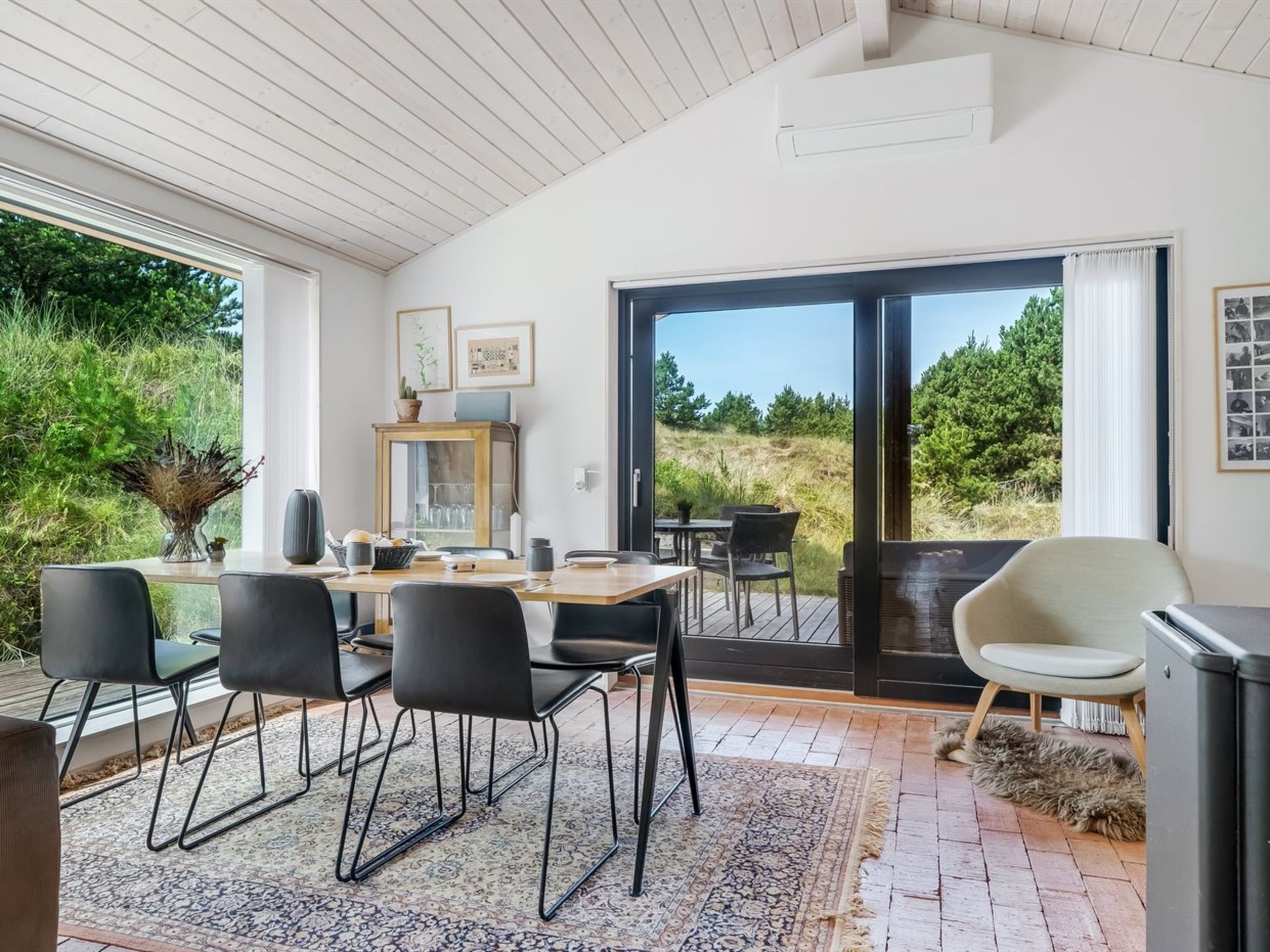 Un comedor moderno con una mesa de madera, sillas negras y vistas al exterior a través de grandes puertas correderas de cristal.