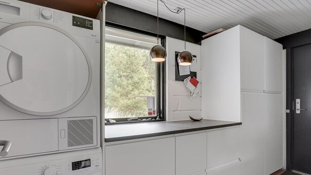 A modern kitchen with a built-in washer and dryer, a window with a view of trees, pendant lights, and white cabinetry. - "Kadife" - 750m from the sea by Interhome (Saltum)