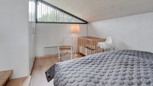 A bedroom with a wooden ceiling, a bed with a grey quilt, a crib, a white chair, and a window with blinds. - "Kadife" - 750m from the sea by Interhome (Saltum)