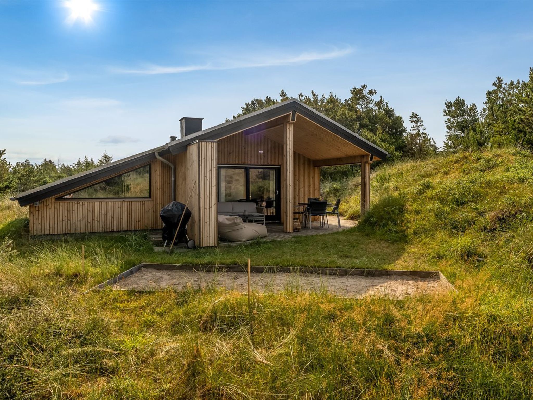 A modern house with a large glass door, a patio with outdoor furniture, and a grassy yard.