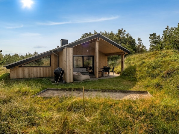 A modern house with a large glass door, a patio with outdoor furniture, and a grassy yard.