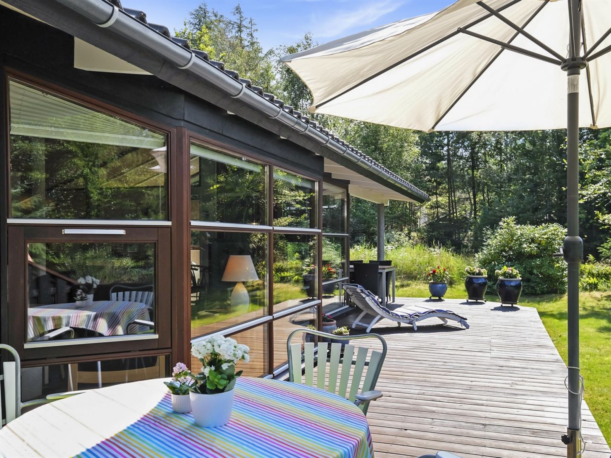 A covered outdoor area with a table and chairs, a large umbrella, and potted plants.