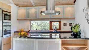 Une cuisine moderne dotée d’un îlot central, d’appareils électroménagers intégrés et d’une grande fenêtre qui laisse entrer la lumière naturelle.