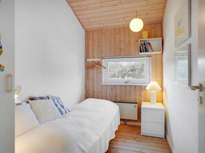 Ein Schlafzimmer mit Bett, Nachttisch, Lampe, Fenster und Holzvertäfelung.