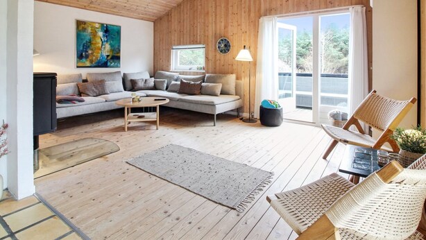 Een knusse woonkamer met een houten plafond, een bank, een bijzettafeltje en een rieten stoel.