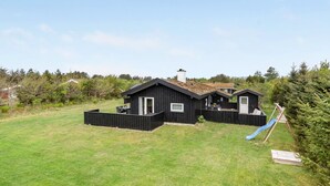 Een zwart houten huis met een omheinde tuin, een glijbaan en een klein terras.