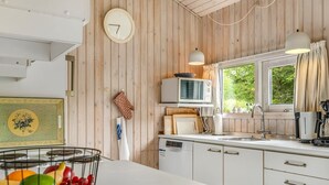 A kitchen with wooden panel walls, a white countertop, a clock, a microwave, a sink, and a fruit bowl.