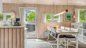 A modern kitchen with wooden paneling, a dining area with white metal chairs, and a view of greenery outside.