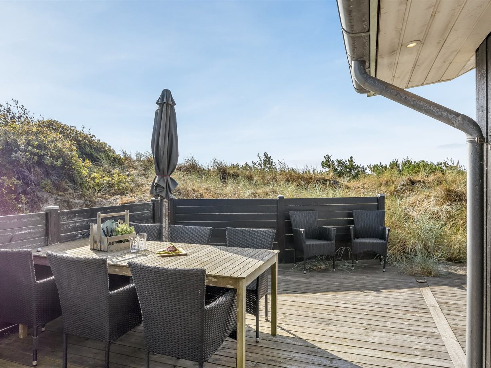 An outdoor patio with a wooden deck, wicker furniture, and a large umbrella.